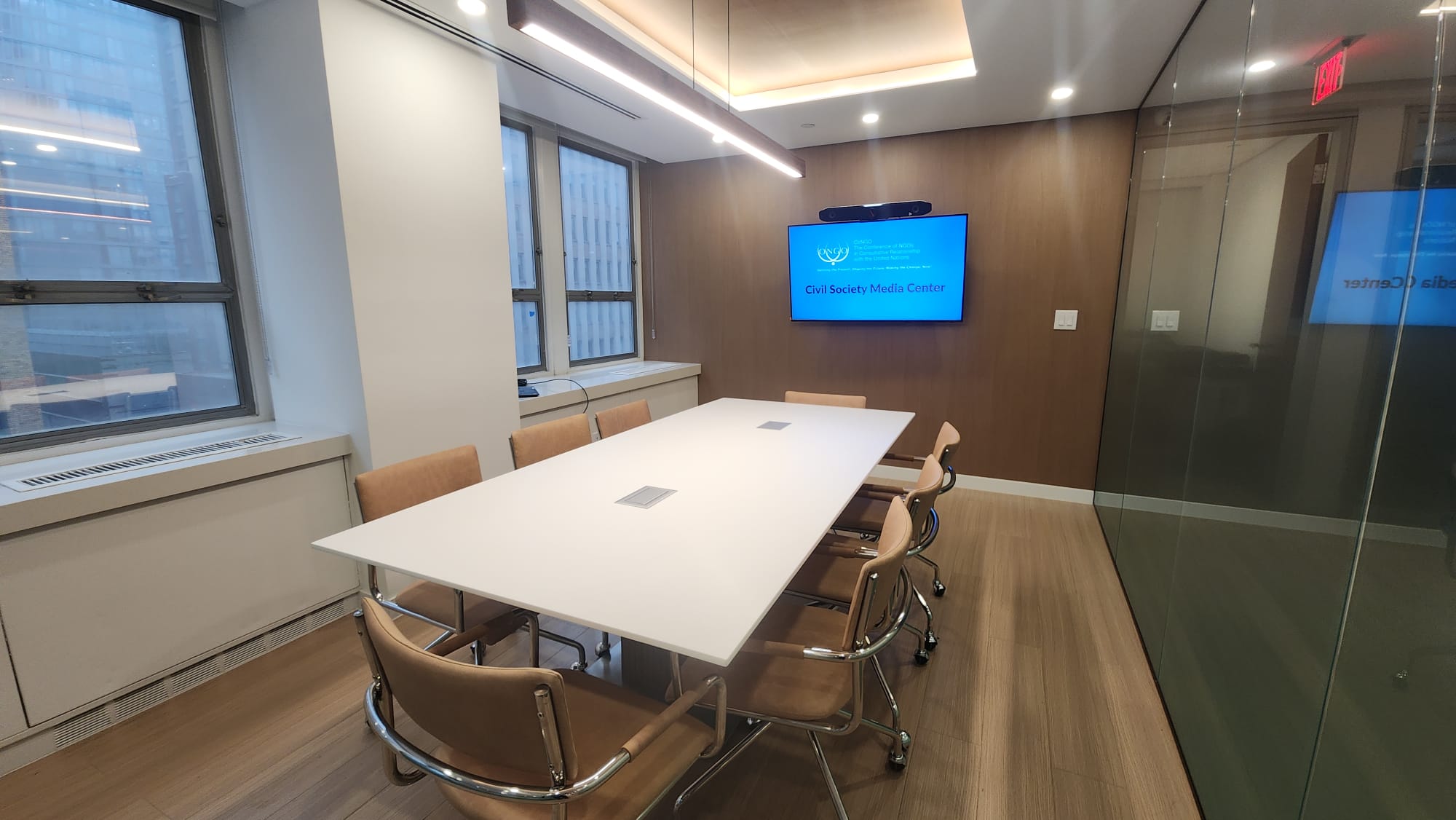 Glass-walled conference room with a large table and wall-mounted display for briefings and interviews